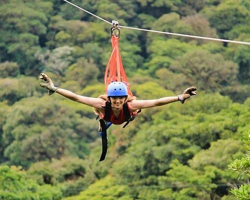 Woman ziplining through lush forest.